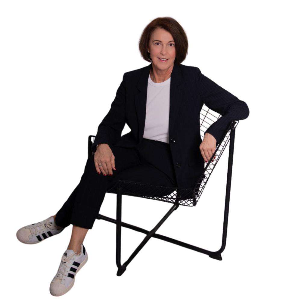 Angelika Schindler-Obenhaus, erfahrene Unternehmensberaterin und Geschäftsführerin von ASO Consulting, sitzt entspannt auf einem modernen Stuhl. Sie trägt ein dunkles Business-Outfit mit weißem T-Shirt und Sportschuhen. Authentisches Business-Porträt für die Website von ASO Consulting.