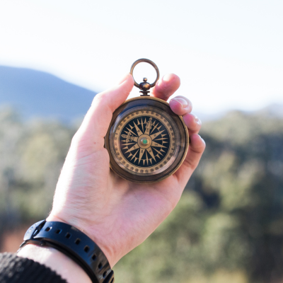 Hand hält einen Kompass mit Blick in eine naturnahe Landschaft – Symbol für Orientierung, Führung und klare Richtung. Sinnbild für die Beratungsphilosophie von ASO Consulting: Menschen und Unternehmen den richtigen Kurs zeigen.