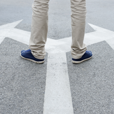Person steht an einer Straßenmarkierung mit Pfeilen in verschiedene Richtungen – Symbol für Entscheidung, Strategie und neue Wege. Metaphorisches Bild für Beratungsprozesse und strategische Orientierung bei ASO Consulting.